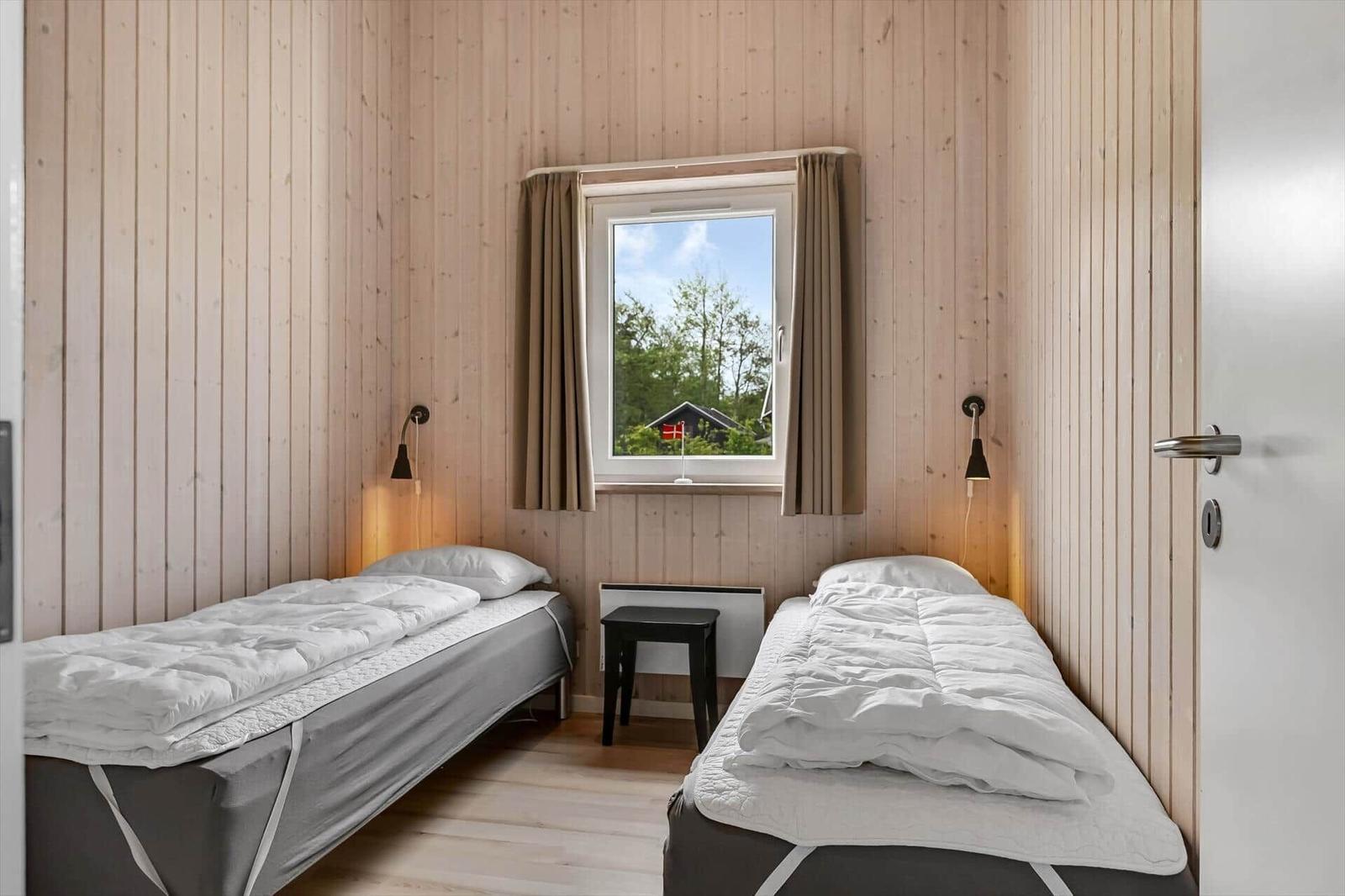 Zwei Einzelbetten, Holzwand, Fenster mit Blick auf Außenbereich.