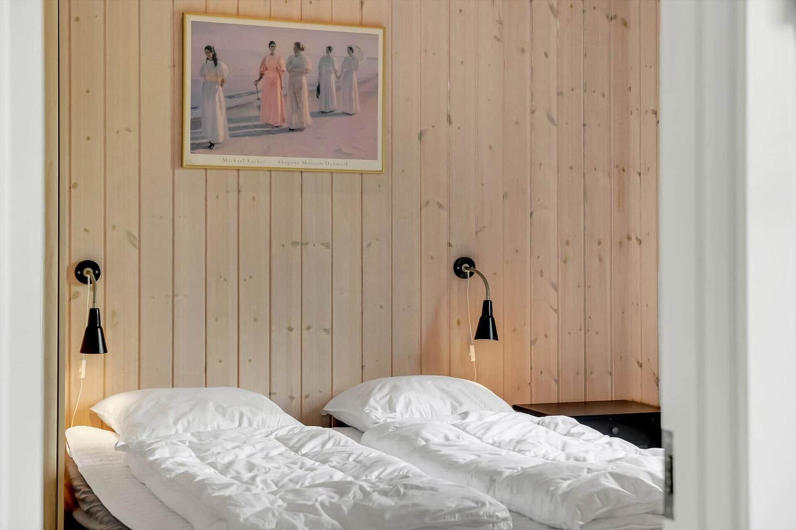 Zwei Betten mit weißen Laken an Holzwand mit Bild und Wandlampen.
