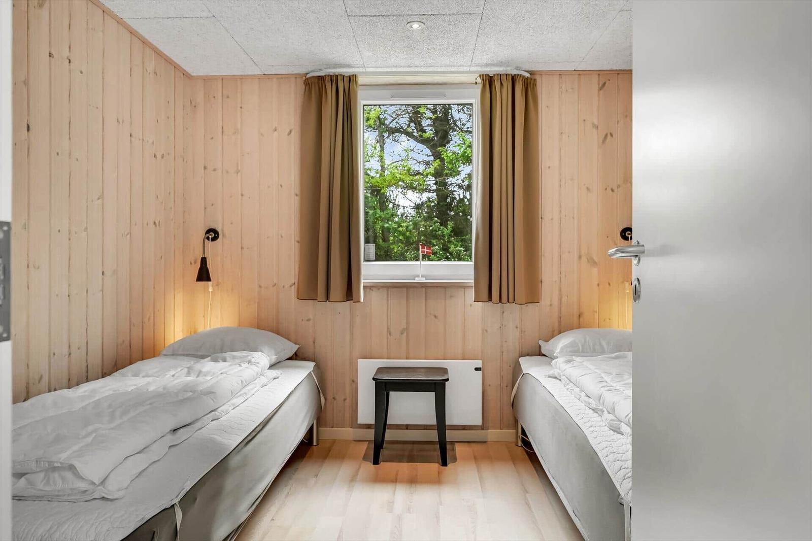 Zwei Betten, Holzwände, Fenster mit Blick auf Bäume und kleine Bank.
