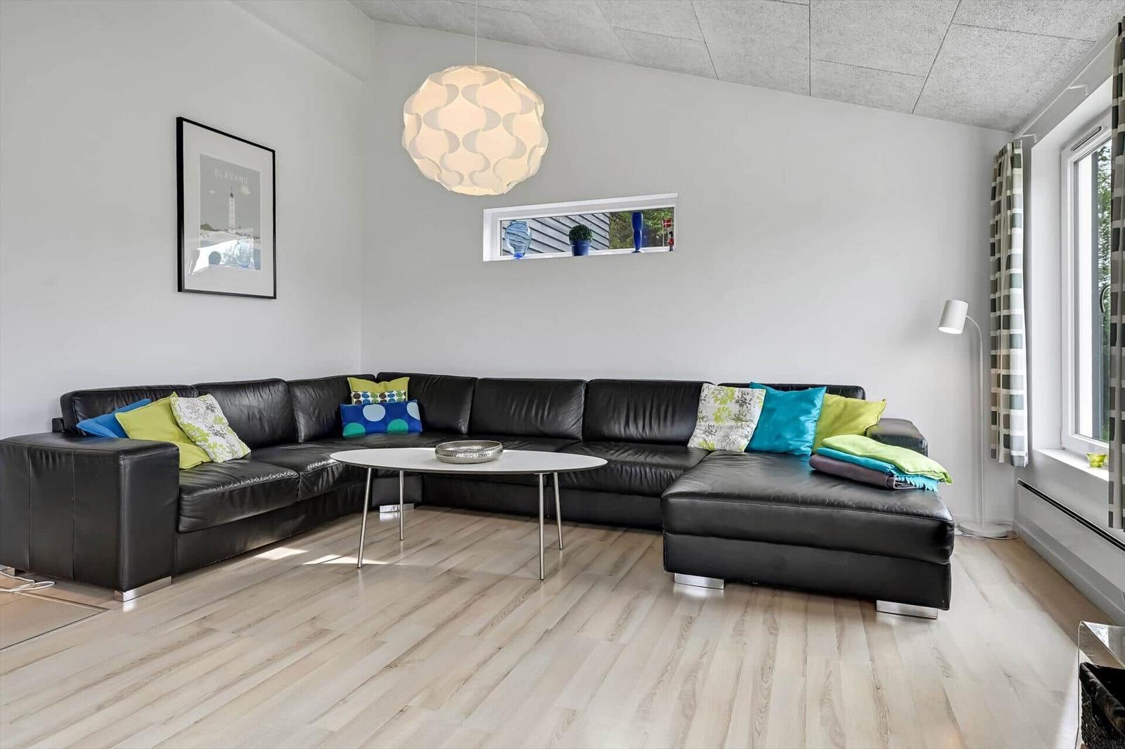 Ein Wohnzimmer mit einem schwarzen Ecksofa, einem runden Tisch und einer Deckenleuchte.