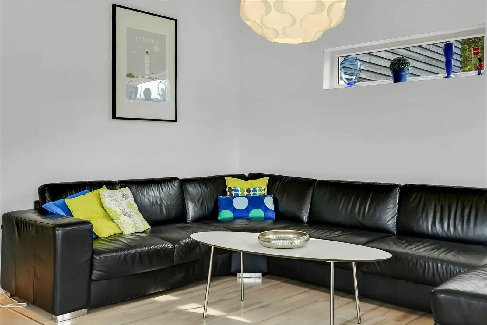 Schwarzes Ledersofa mit bunten Kissen, runder Tisch und Fenster mit Blick nach draußen.