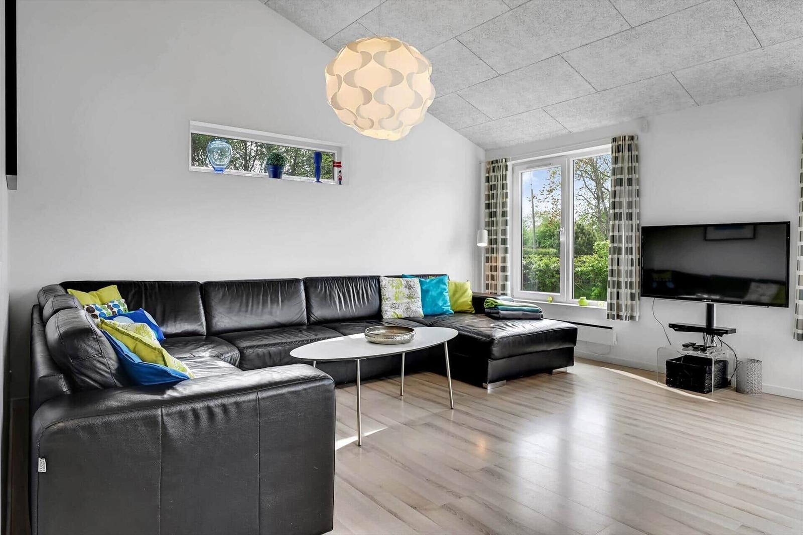 Wohnzimmer mit schwarzer Ledercouch, Holzboden und Fernseher an der Wand.
