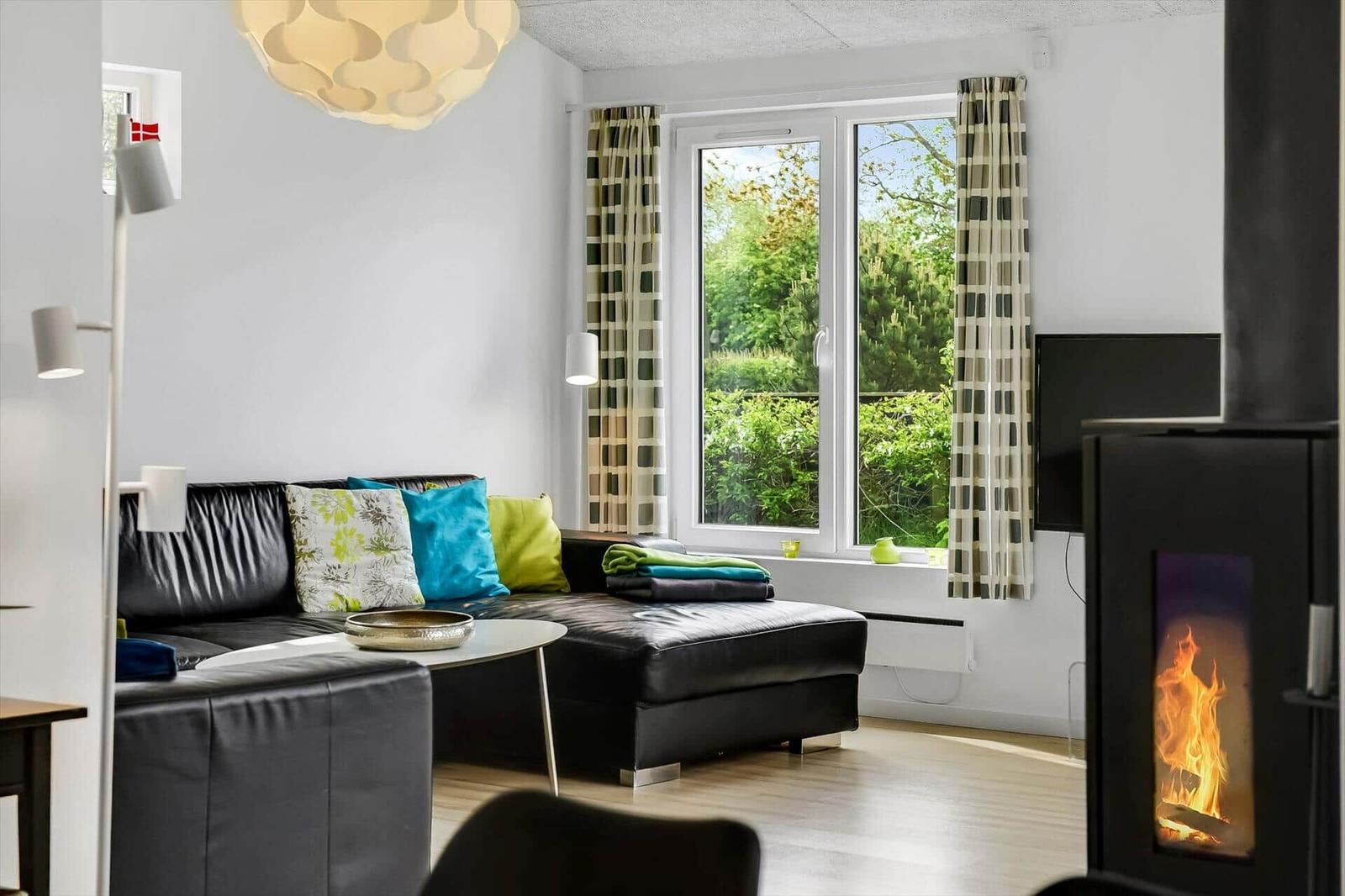 Wohnzimmer mit Sofa, Kamin und Fensterblick auf Grünflächen.