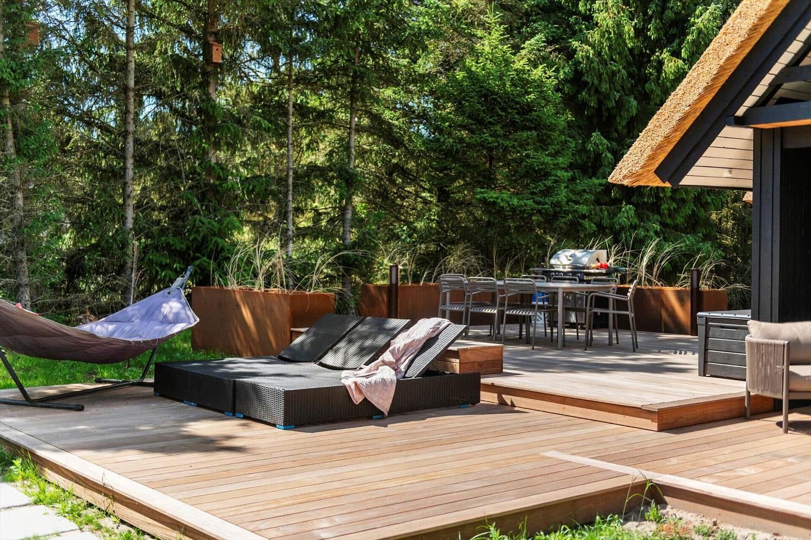 Holzterrasse mit Liege, Hängematte und Grillplatz im Wald.