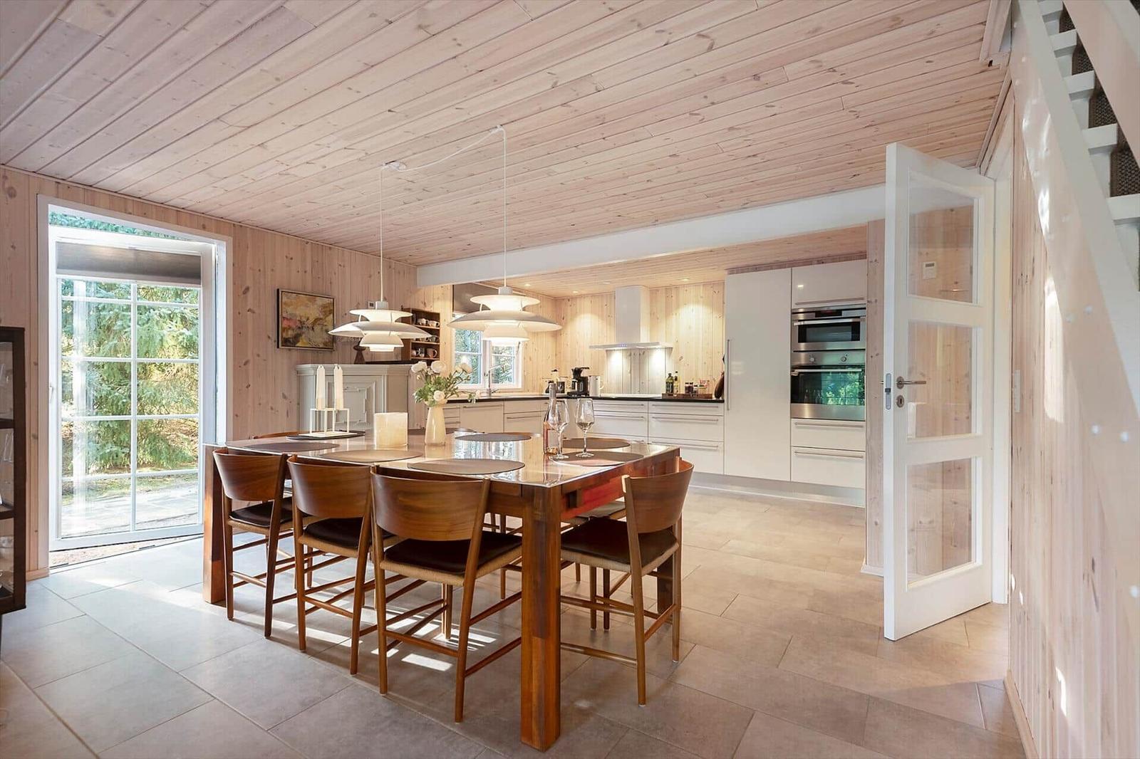 Essbereich mit Holztisch und Stühlen. Küche mit Edelstahlgeräten und Holzwand.
