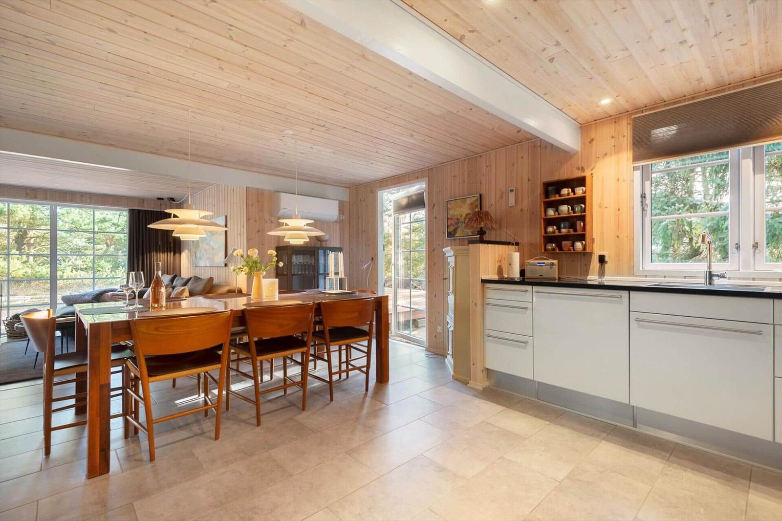 Küche und Essbereich mit Holzdecke, weißen Schränken und Holztisch mit Stühlen.