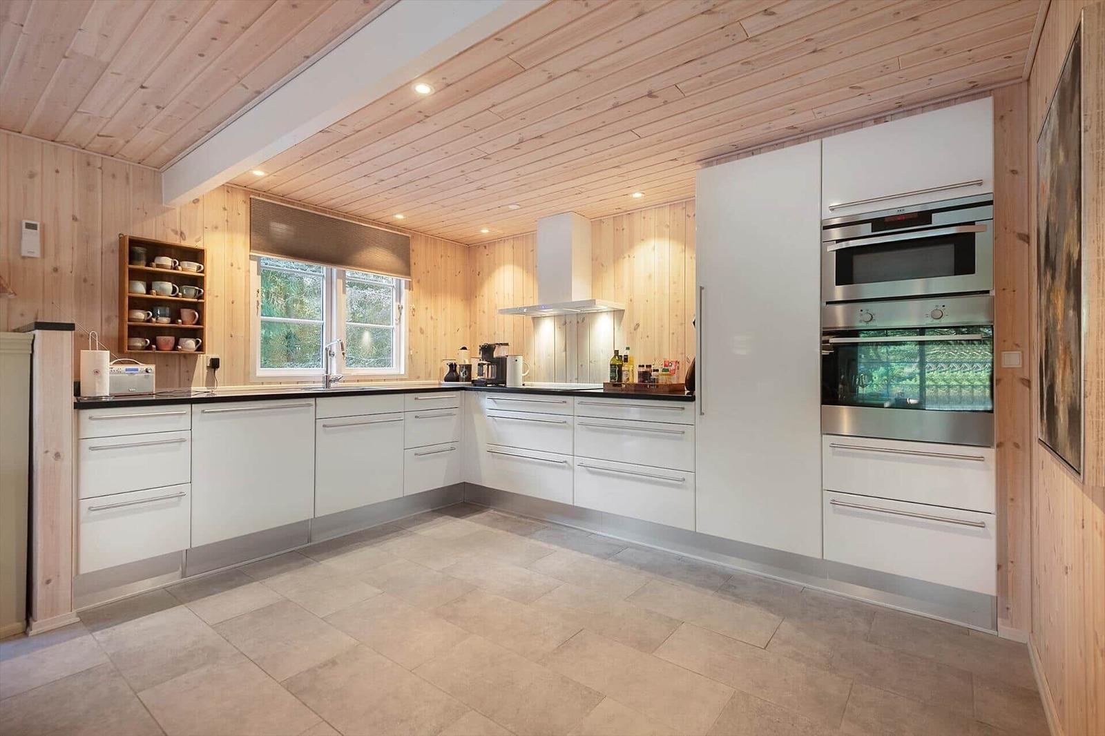 Moderne Küche mit weißen Schränken, Holzwand und -decke, integriertem Ofen und Fenster.