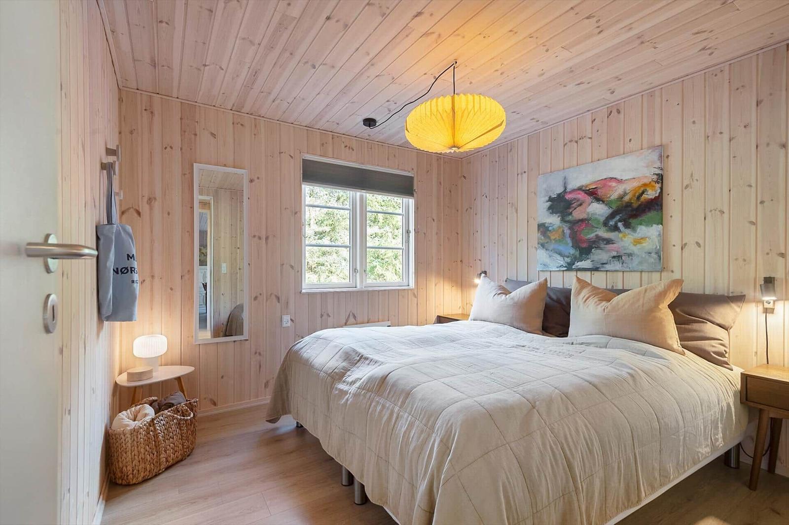 Schlafzimmer mit Holzwand, Bett, Fenster und Deckenleuchte.