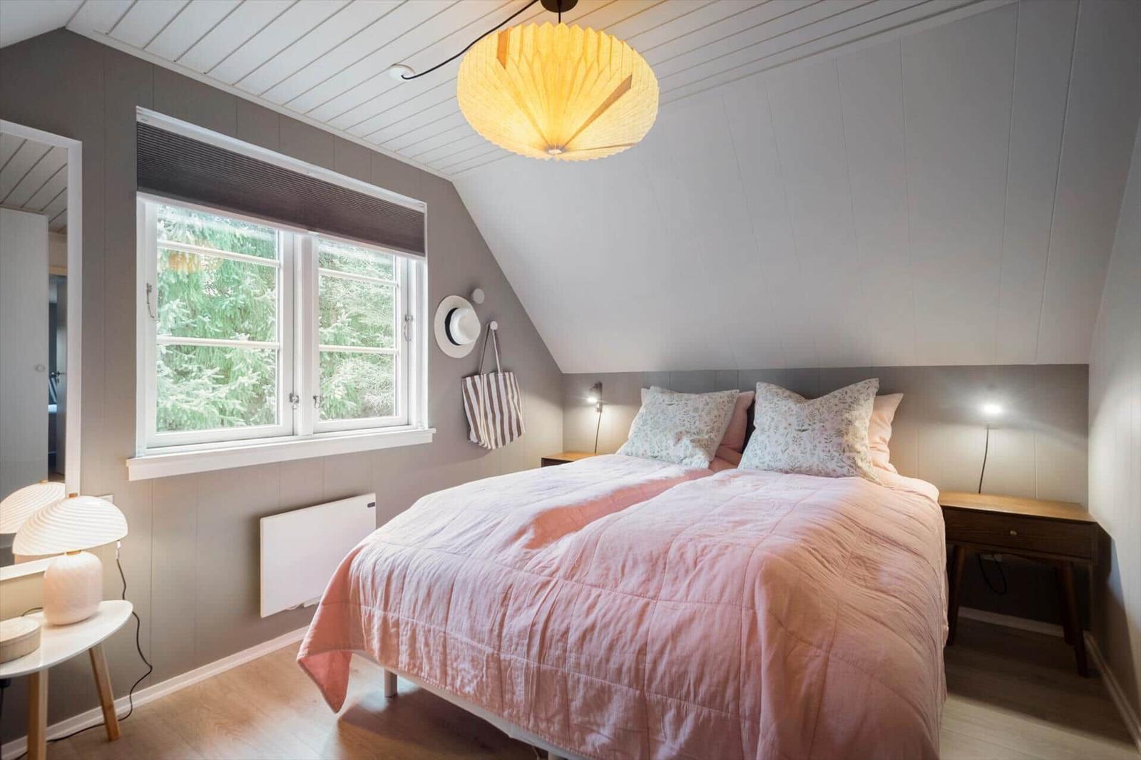 Schlafzimmer mit Dachschräge, Bett mit rosa Bettwäsche, Fenster mit Blick auf Bäume.