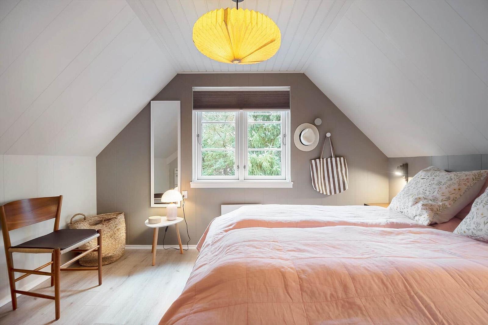 Schlafzimmer mit Dachschrägen, Bett, Fenster und Lampe.