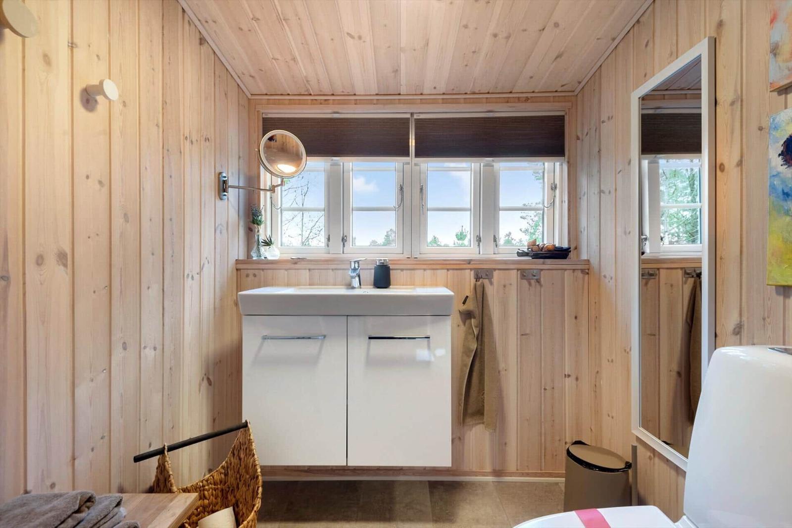 Badezimmer mit Holzwand, Waschbecken und Fenster mit Blick auf Außengelände.