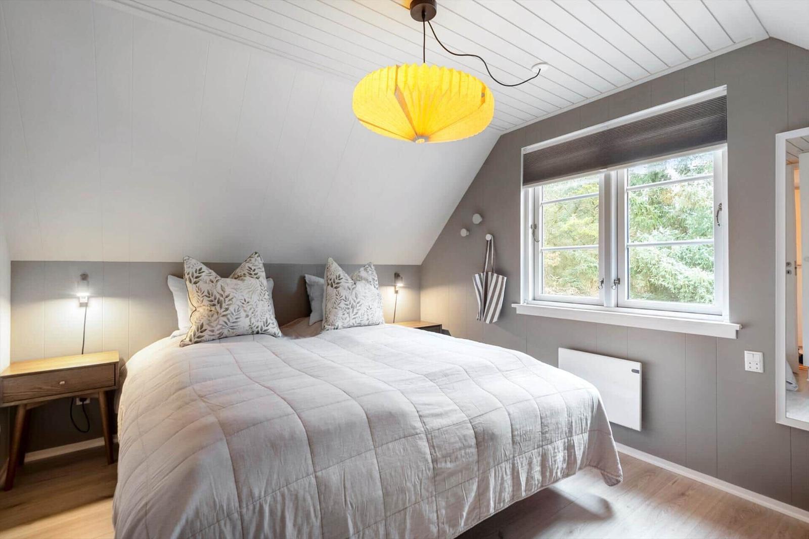 Schlafzimmer mit Dachschrägen, großem Bett und Fenster mit Blick auf Bäume.