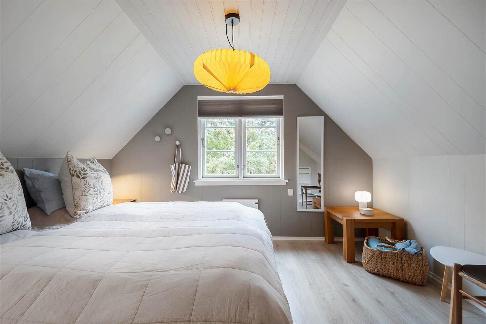 Schlafzimmer mit Dachschrägen, Bett, Fenster und Nachttisch.