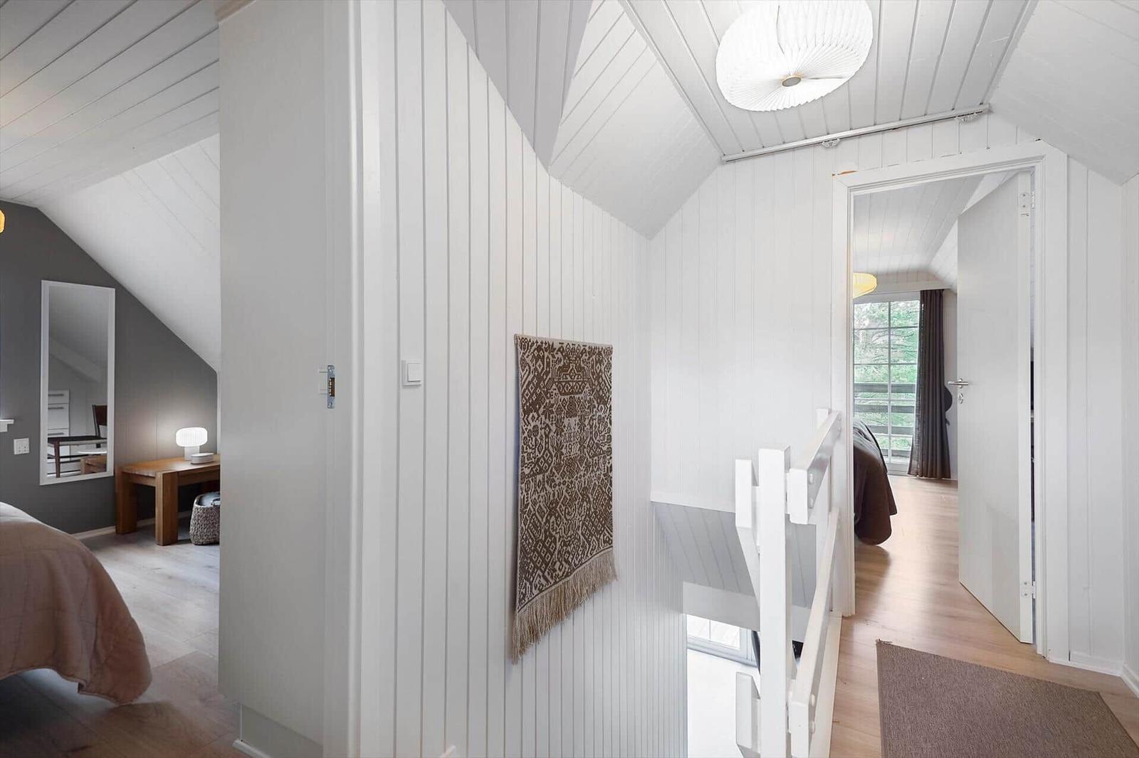 Durchgang mit weiß verkleideten Wänden und Holzboden. Tür führt in Schlafzimmer. Wandteppich hängt an Wand.