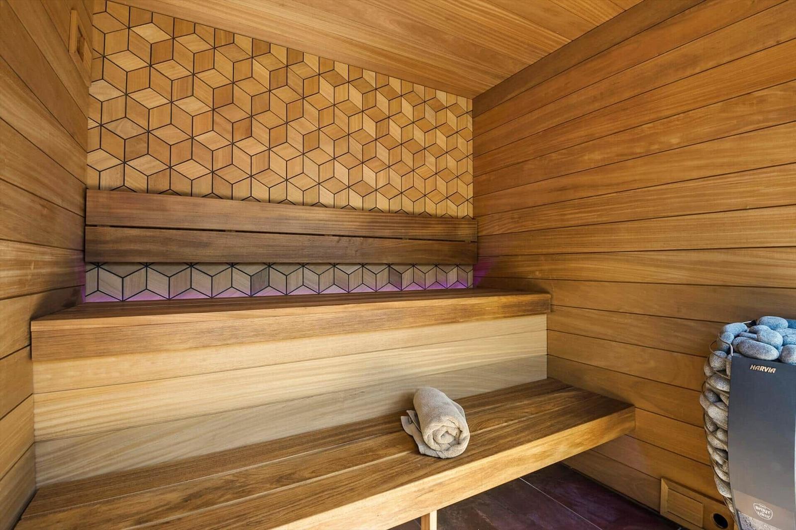 Sauna mit Holzbank, geometrischer Wandverkleidung und gefalteter Handtuchrolle.