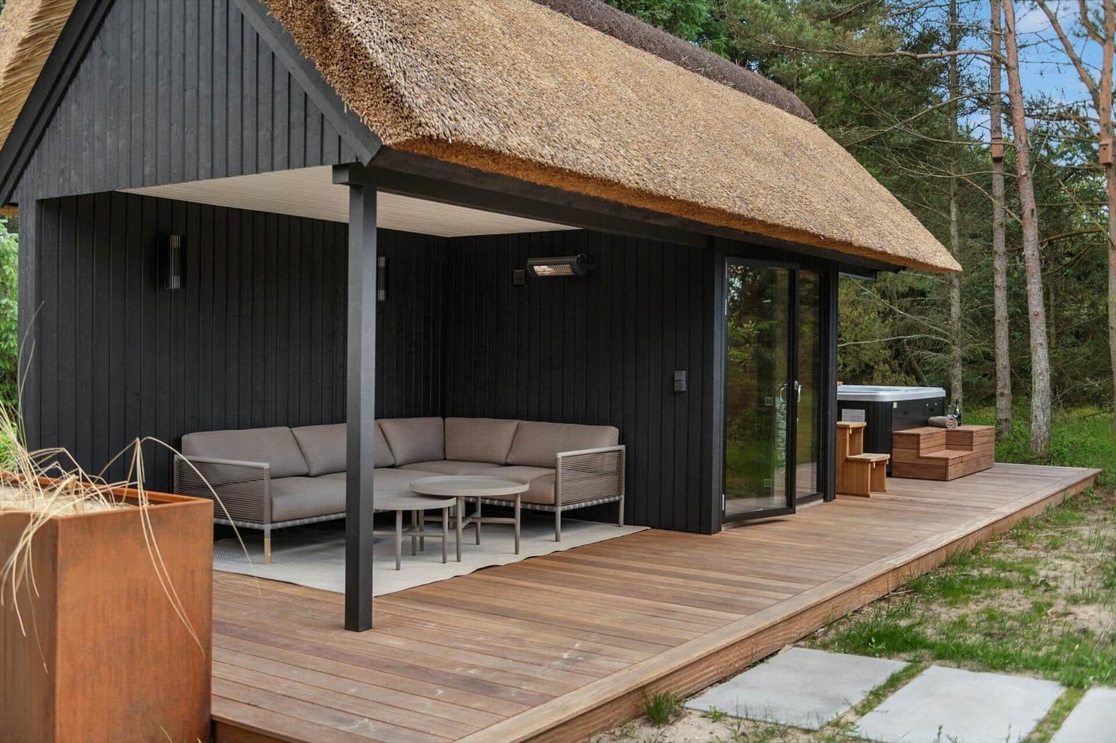 Hütte mit Holzterrasse, Dach aus Stroh und Außensitzbereich mit Sofa.