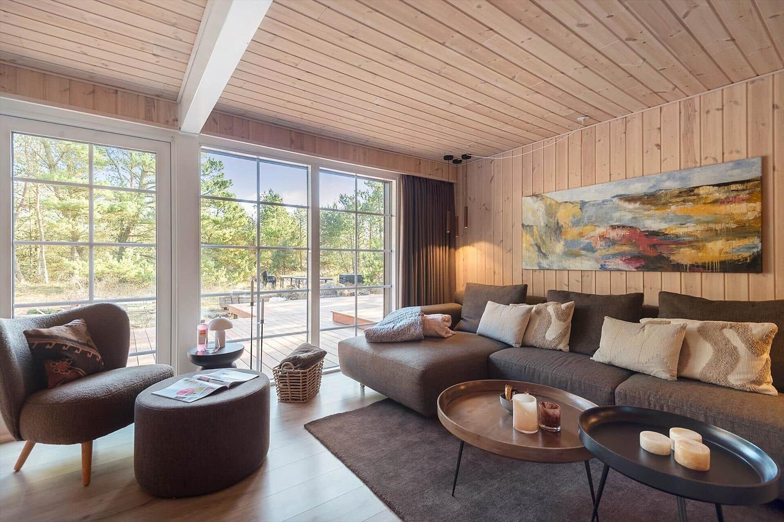 Wohnzimmer mit Holzwand, großem Sofa und Blick auf Balkon und Wald.