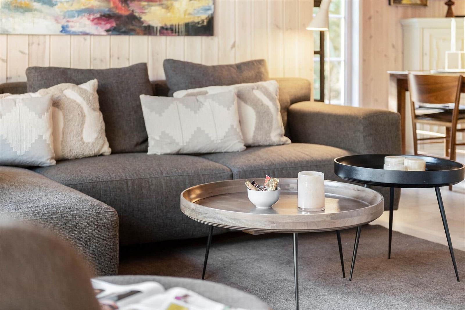 Ein Wohnzimmer mit grauem Sofa, dekorativen Kissen und zwei runden Tischen.