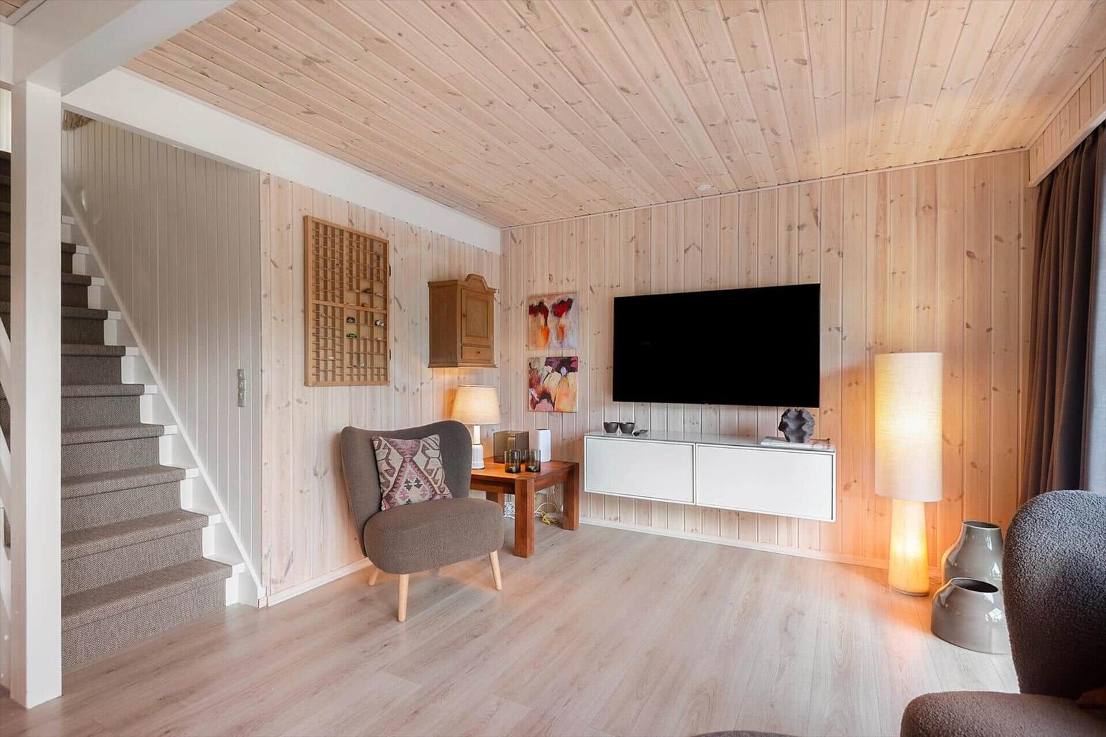 Wohnzimmer mit Holzwand, TV, Sessel und Treppe