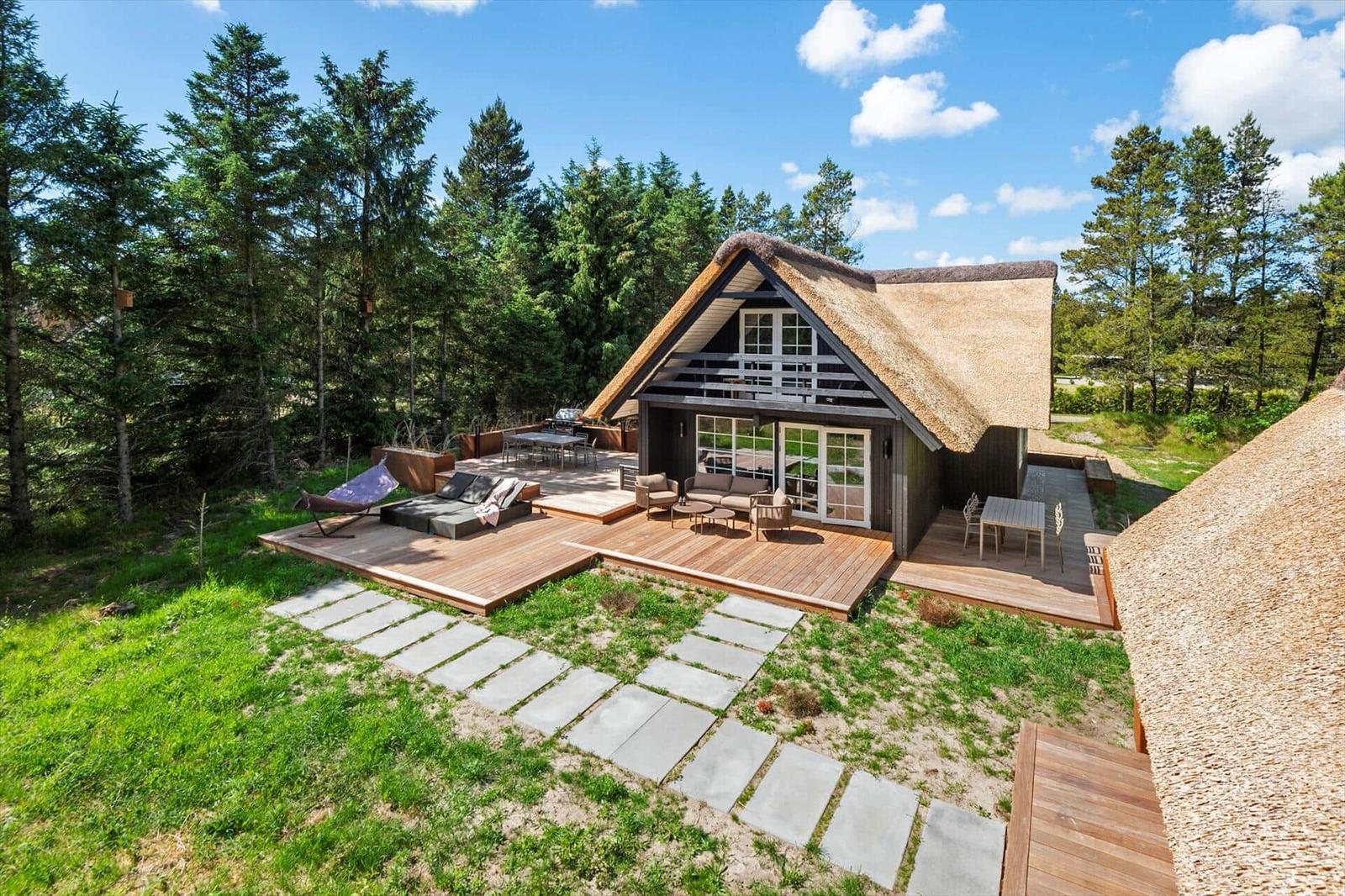 Haus mit strohgedecktem Dach und großem Holzterrasse im Wald