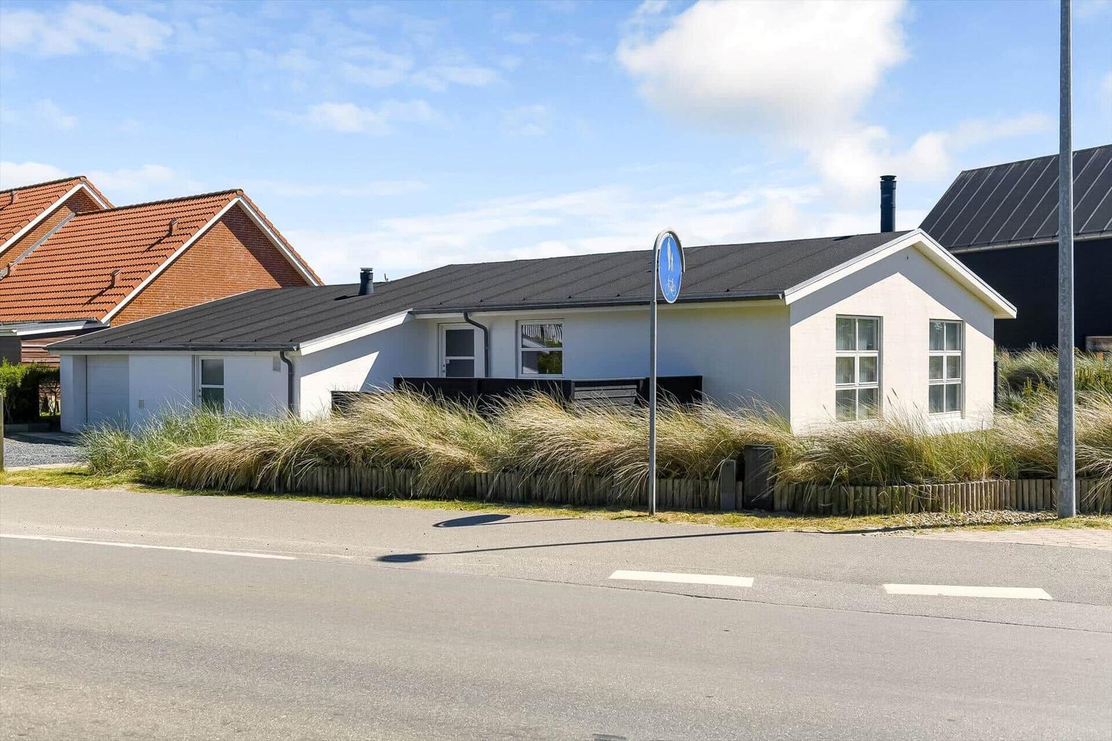 Wohnhaus mit dunklem Dach und weißen Wänden, umgeben von Gras und einer Straße.