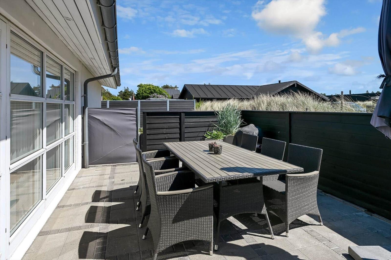 Terrasse mit Tisch und Stühlen, umgeben von dunklem Holzzaun und Pflanzen.