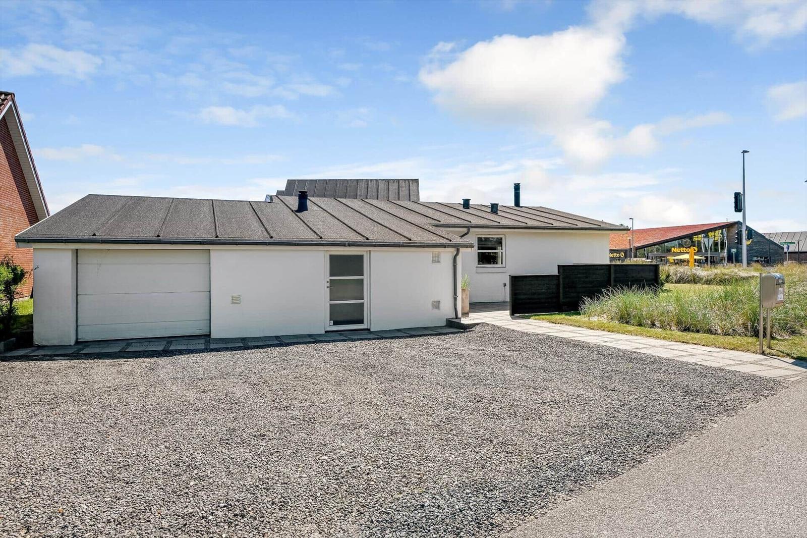 Ein weißes Einfamilienhaus mit Garage und Kiesfläche unter blauem Himmel.