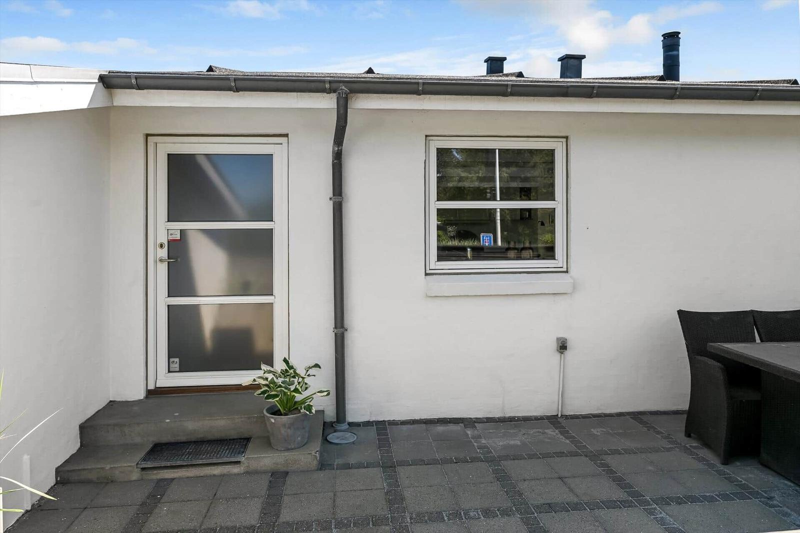 Haus mit Eingangstür, Fenster und Terrasse mit Tisch und Stühlen.