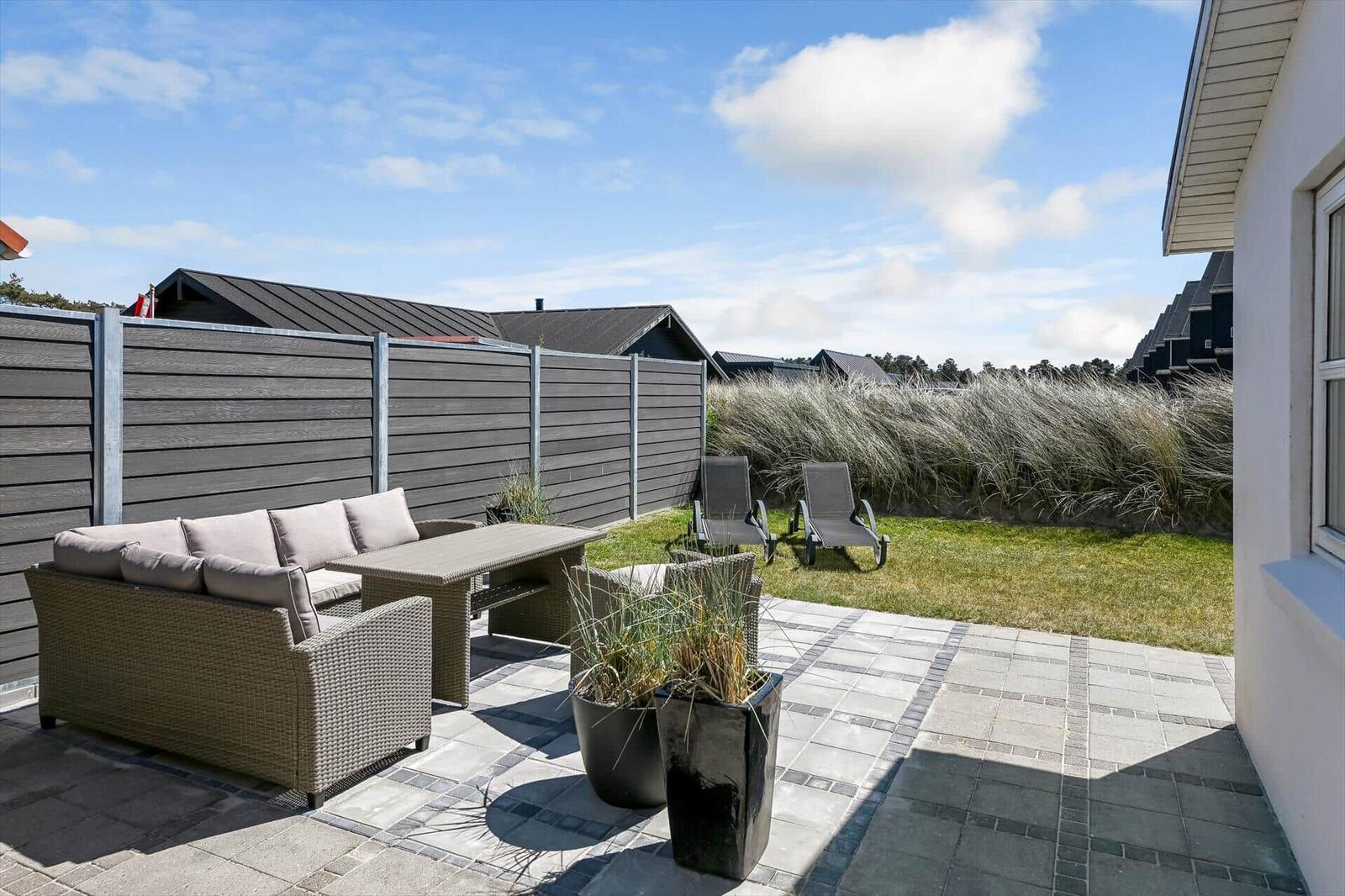 Terrasse mit Sitzgruppe, Liegestühlen und Grasfläche hinter Holzabsperrung.