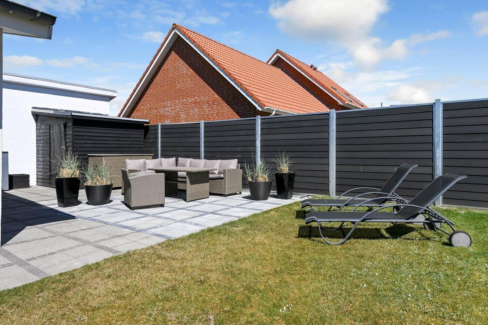 Hinterhof mit Terrasse, Gartenliegen und Sitzgruppe. Schwarze Hecke und roter Dachfirst.