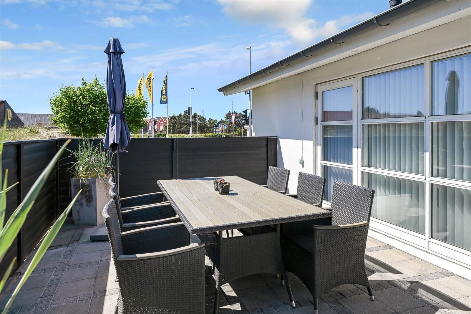 Terrasse mit Tisch und Stühlen, Sonnenschirm und Pflanzen. Hinterhof mit Zaun und Fenster.