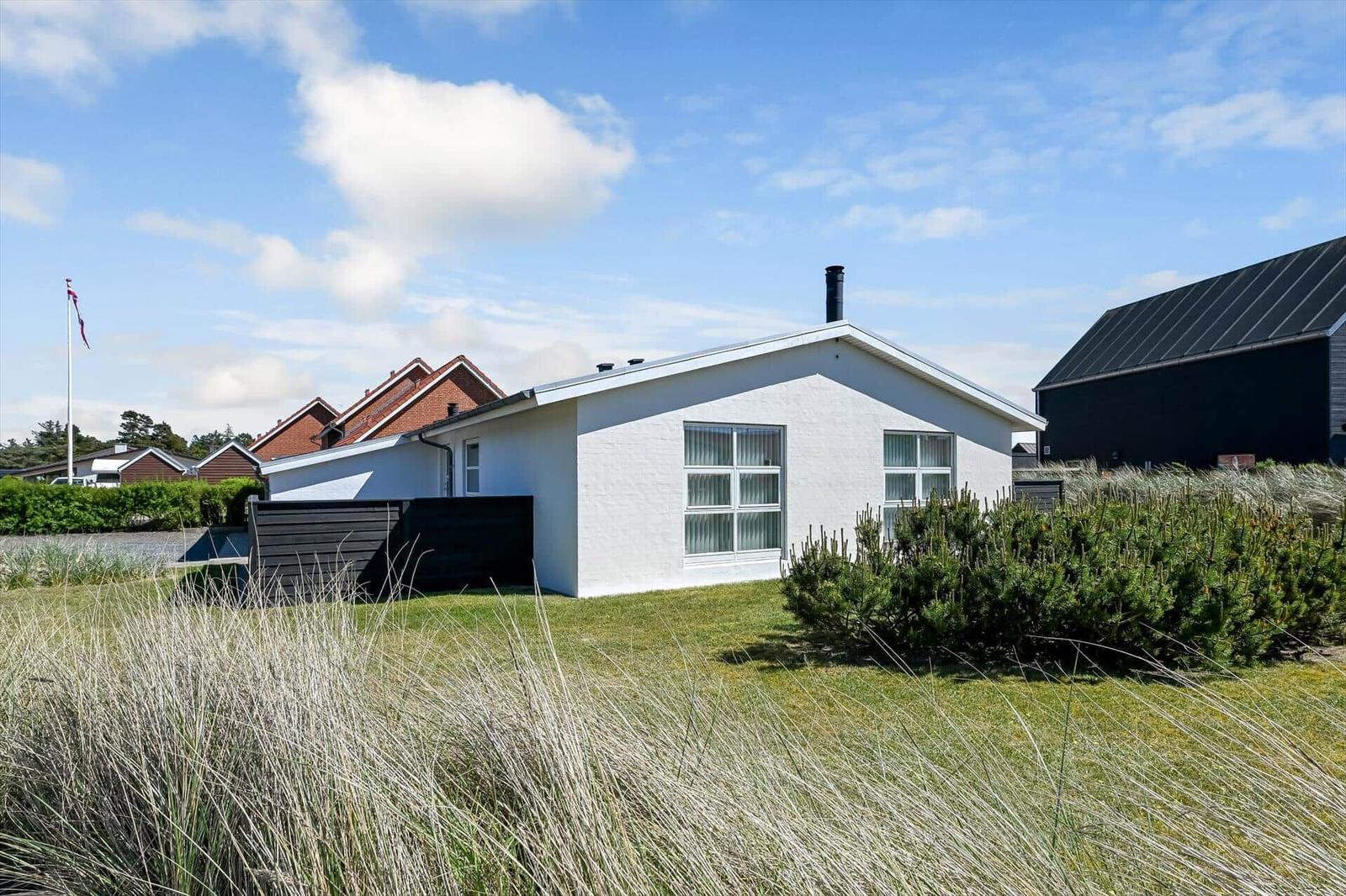 Weiße Ferienhaus mit Garten und Flagge unter blauem Himmel