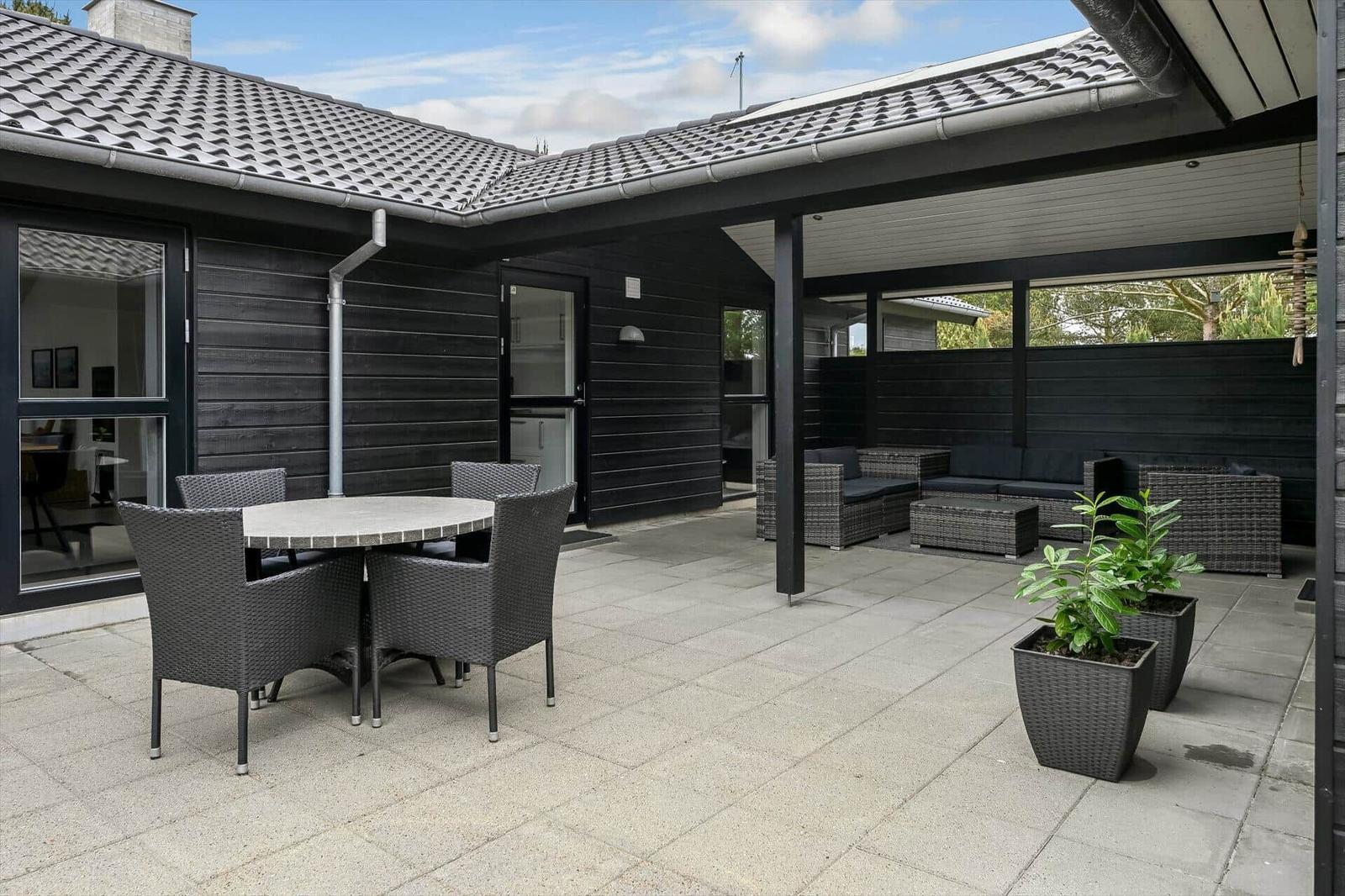 Terrasse mit Sitzgruppe, Tisch und Stühlen. Schwarze Holzwand und Dachüberstand.
