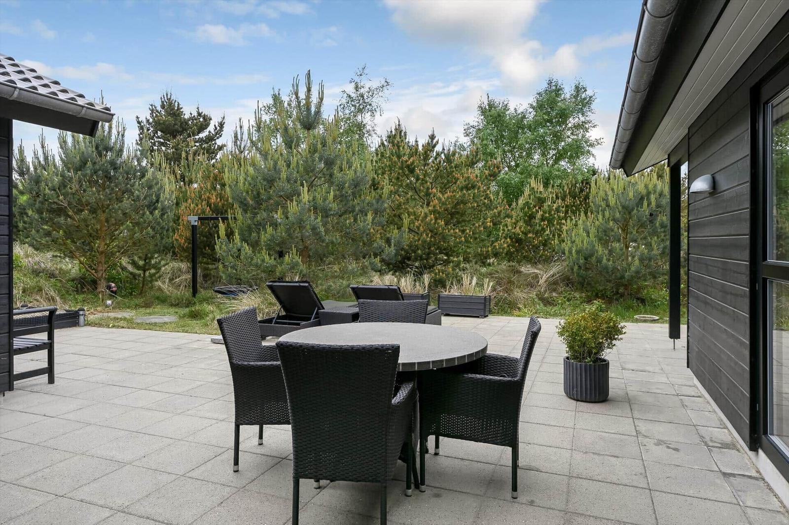 Terrasse mit Tisch und Stühlen, umgeben von Bäumen und Pflanzen.