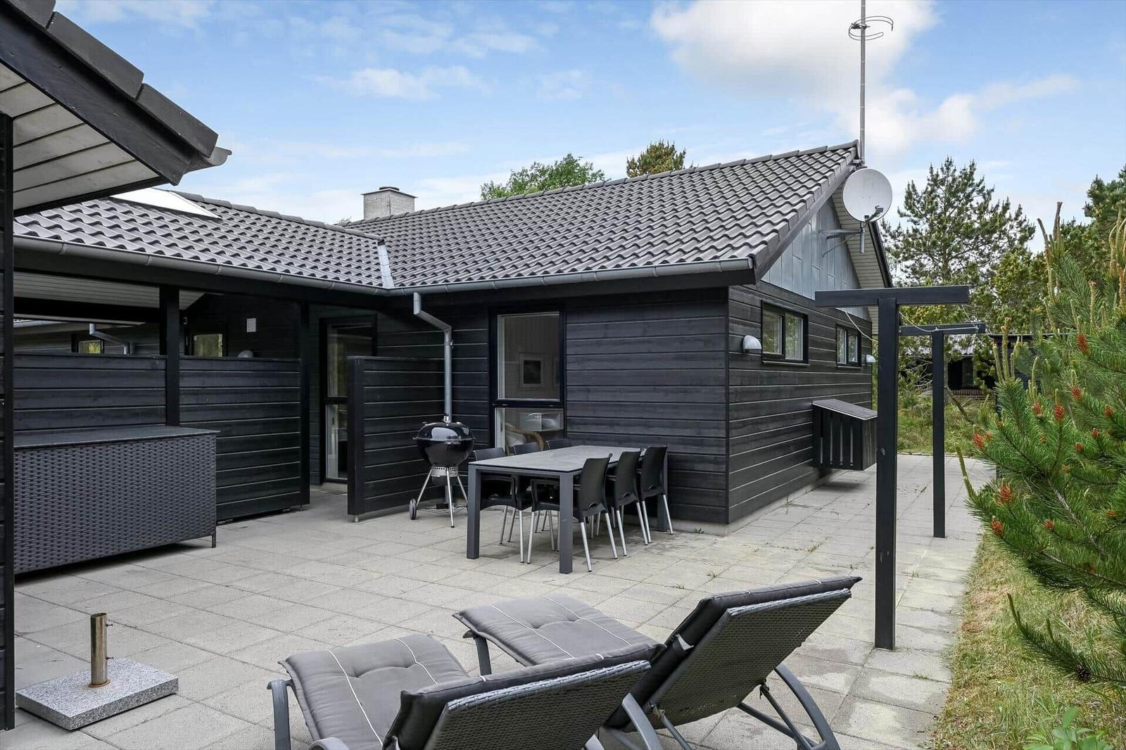 Gartenhaus mit Terrasse, Grill und Liegestühlen. Holzwand und Dachziegel sichtbar.