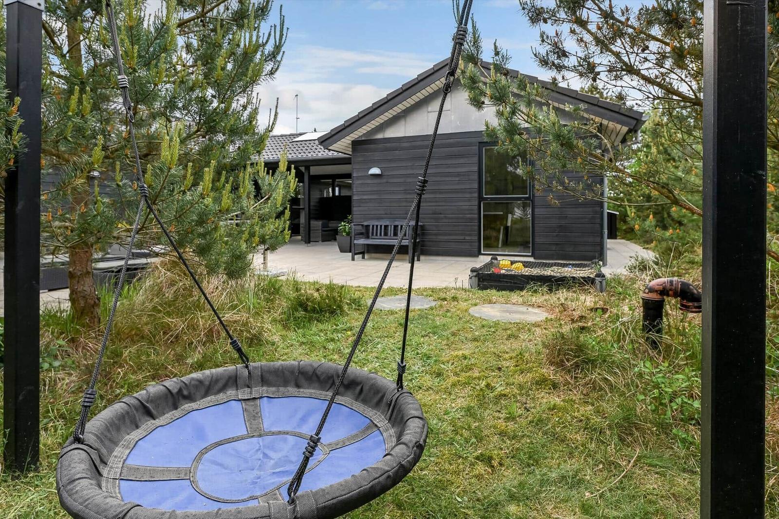Haus mit Balkon, Schaukel und Garten. Modernes Design mit dunkler Fassade.