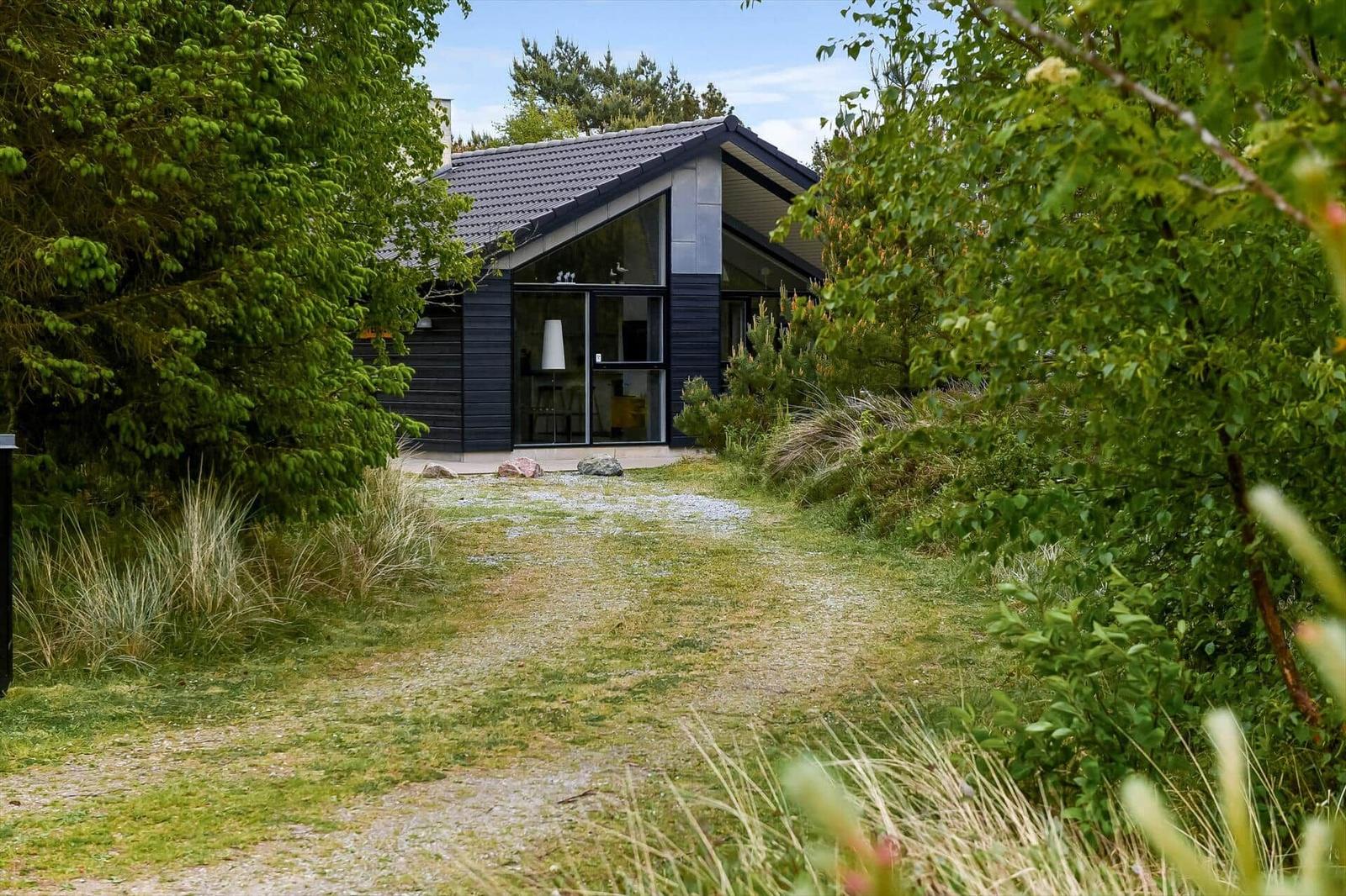 Moderne Villa mit großem Glasbereich, umgeben von grüner Vegetation und einem gepflasterten Weg.