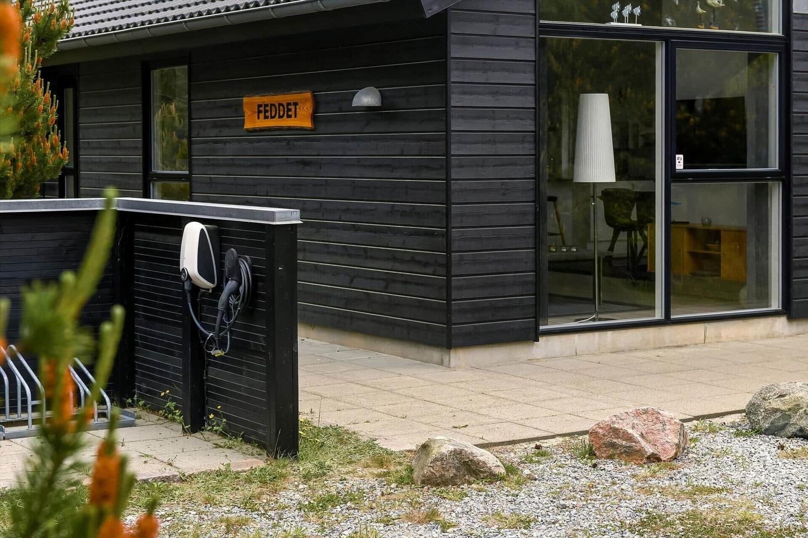 Schwarzes Holzhaus mit Glasfront, Ladekabel und Schild FEDDET.