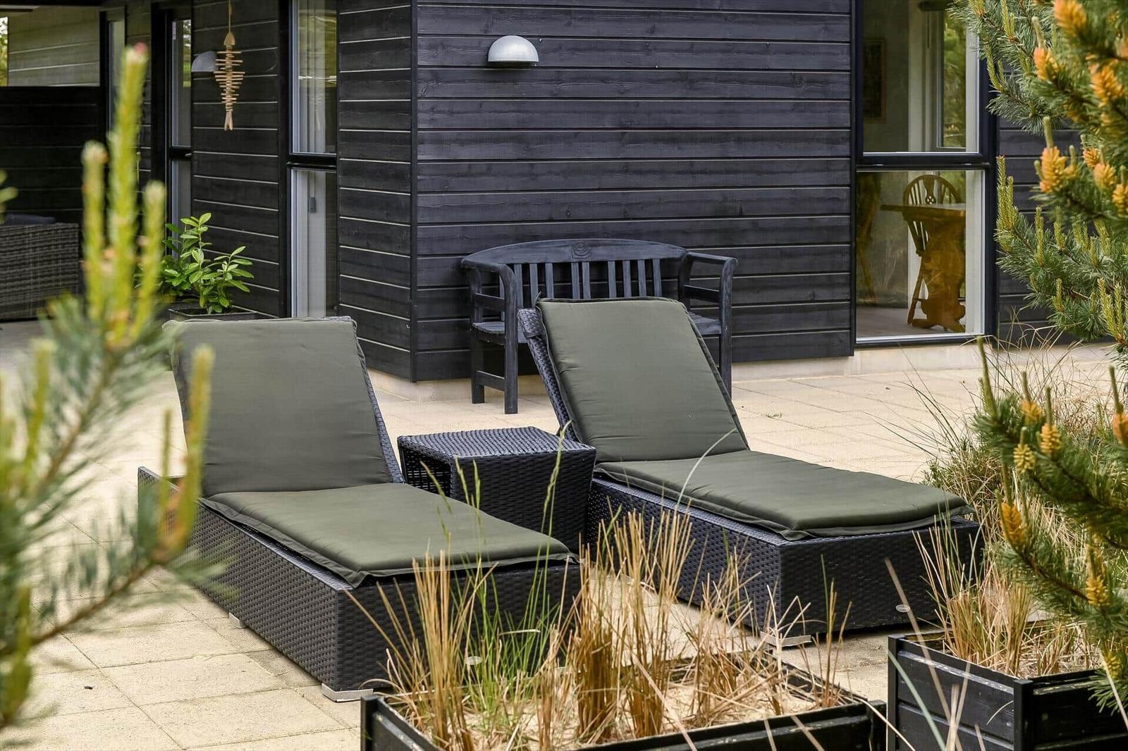 Zwei Liegestühle mit Kissen stehen auf einer Terrasse vor einem Haus mit dunklem Holz.