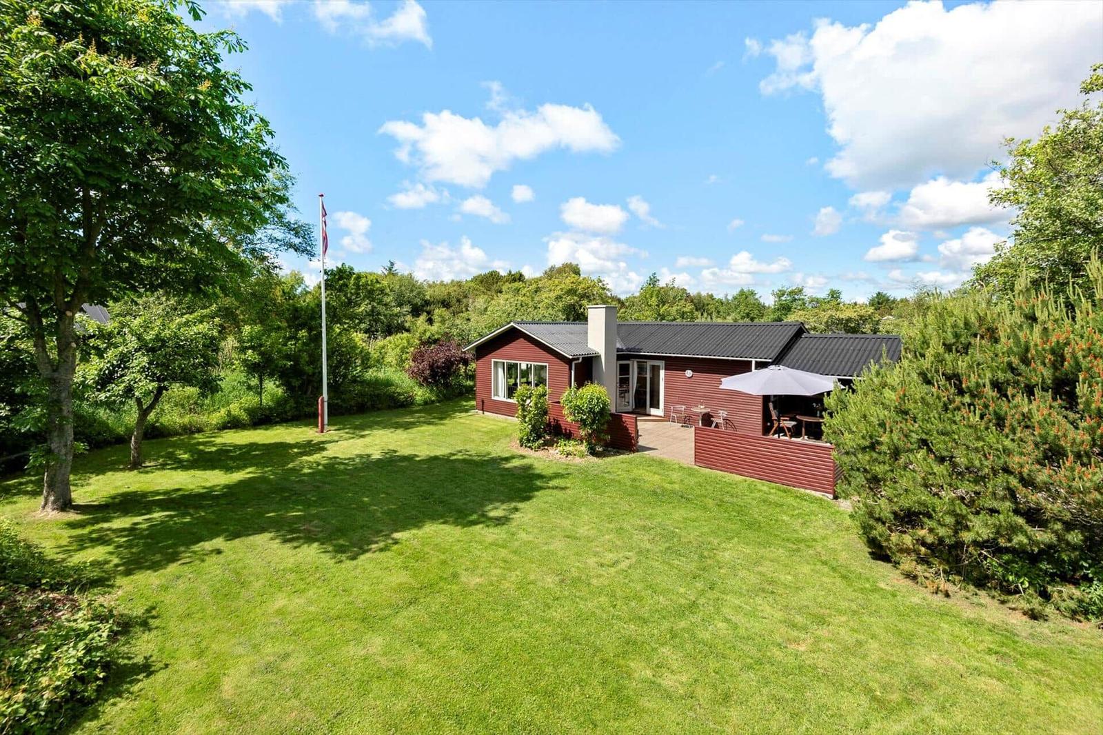 Rotes Ferienhaus mit Garten und Terrasse unter blauem Himmel.
