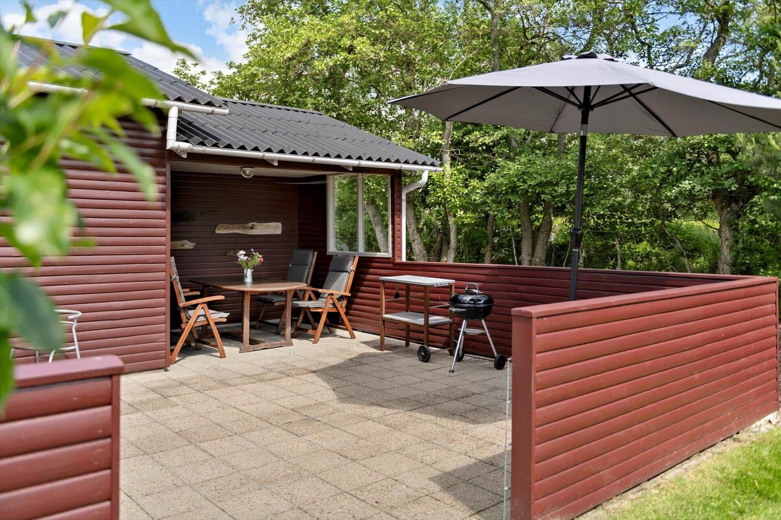 Terrasse mit Tisch, Stühlen, Grill und Sonnenschirm neben Holzhaus.