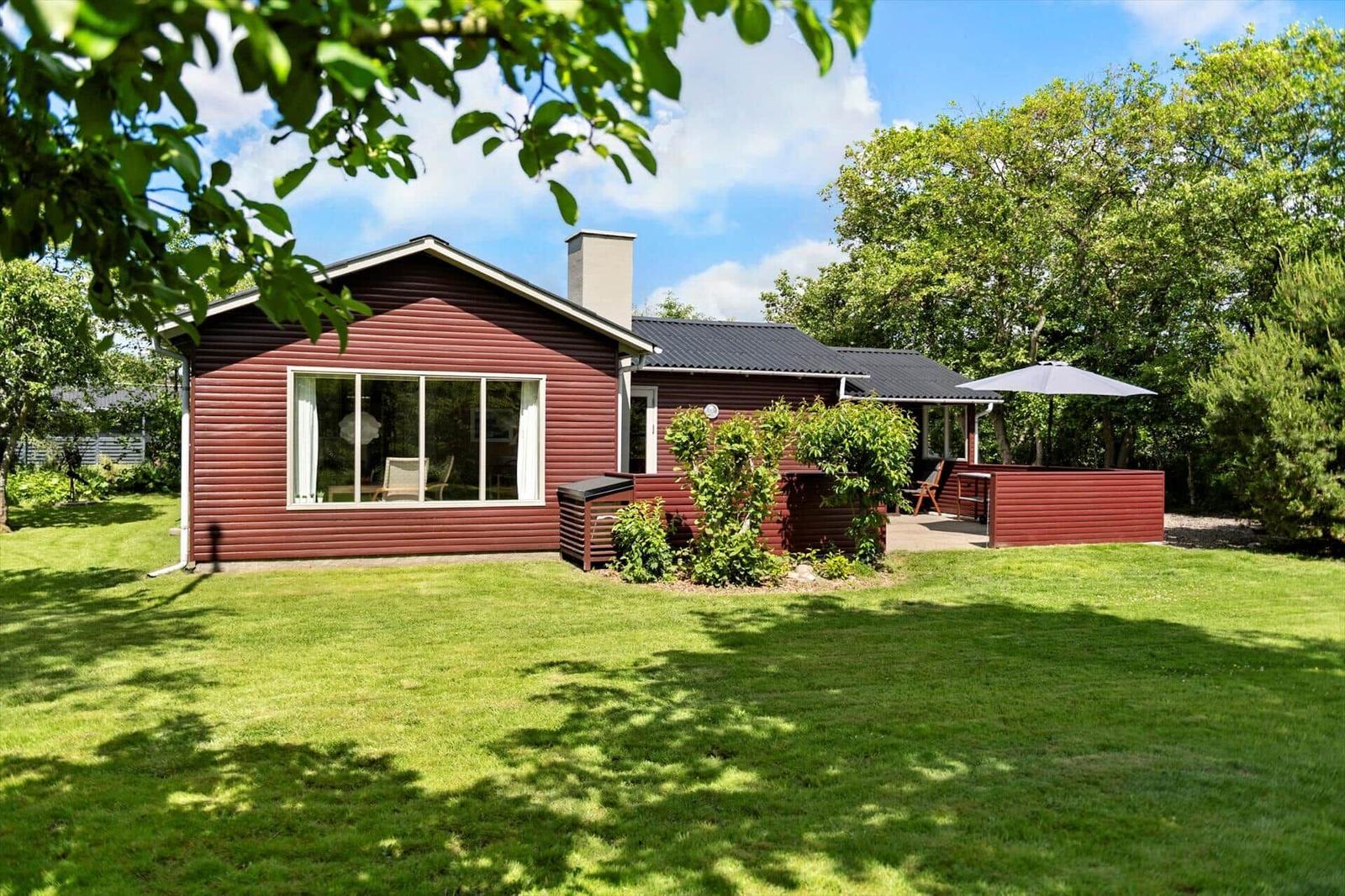 Rotes Holzhaus mit großem Garten und Terrasse unter Bäumen.