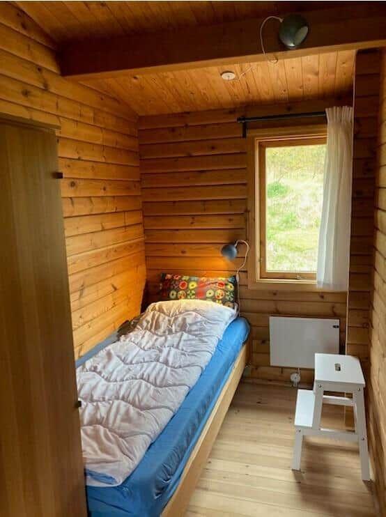 A bedroom with wooden walls, bed, window, and chair.
