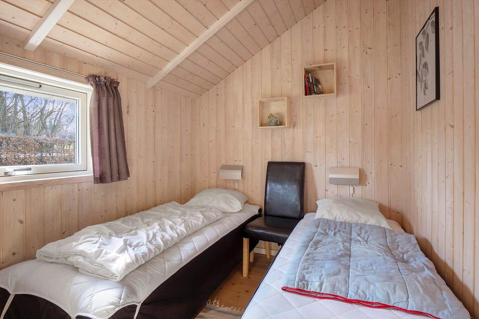 Zwei Betten in einem Holzraum mit Fenster und Wandregalen.