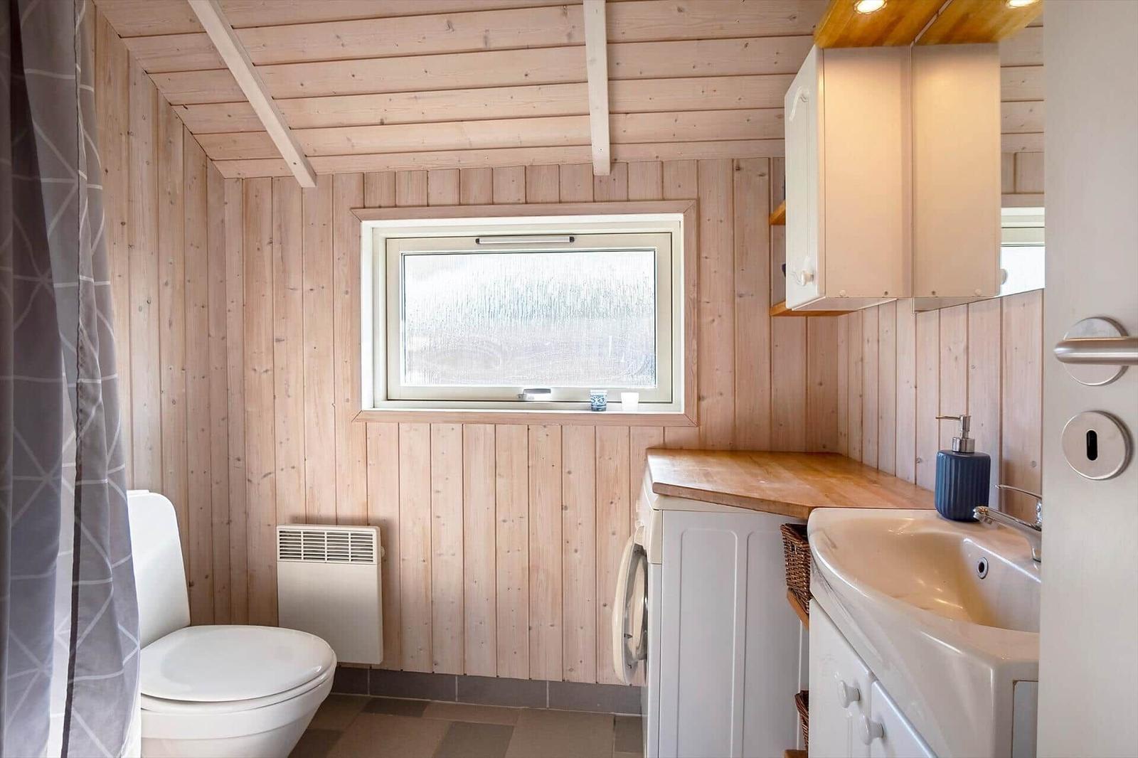 Badezimmer mit Toilette, Waschbecken und Fenster. Holzwände und weiße Möbel.
