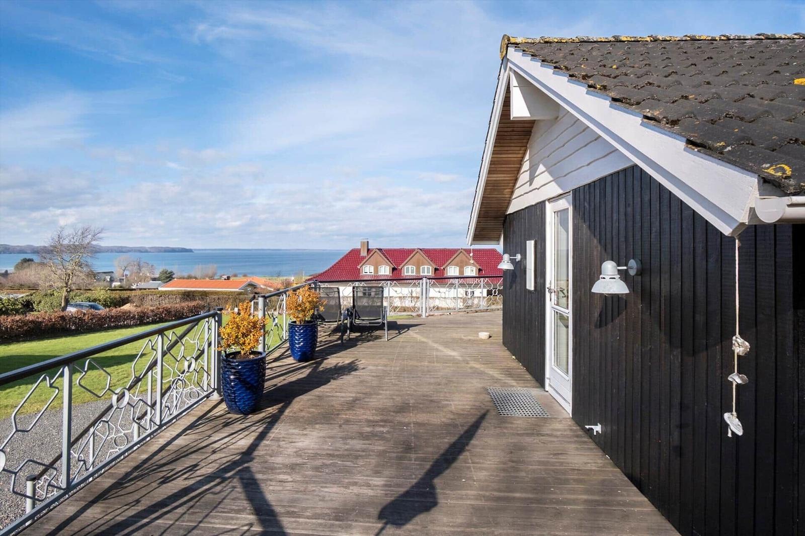 Terrasse mit Blick auf See und rote Dächer. Schwarze Fassade und blaue Pflanzkübel.