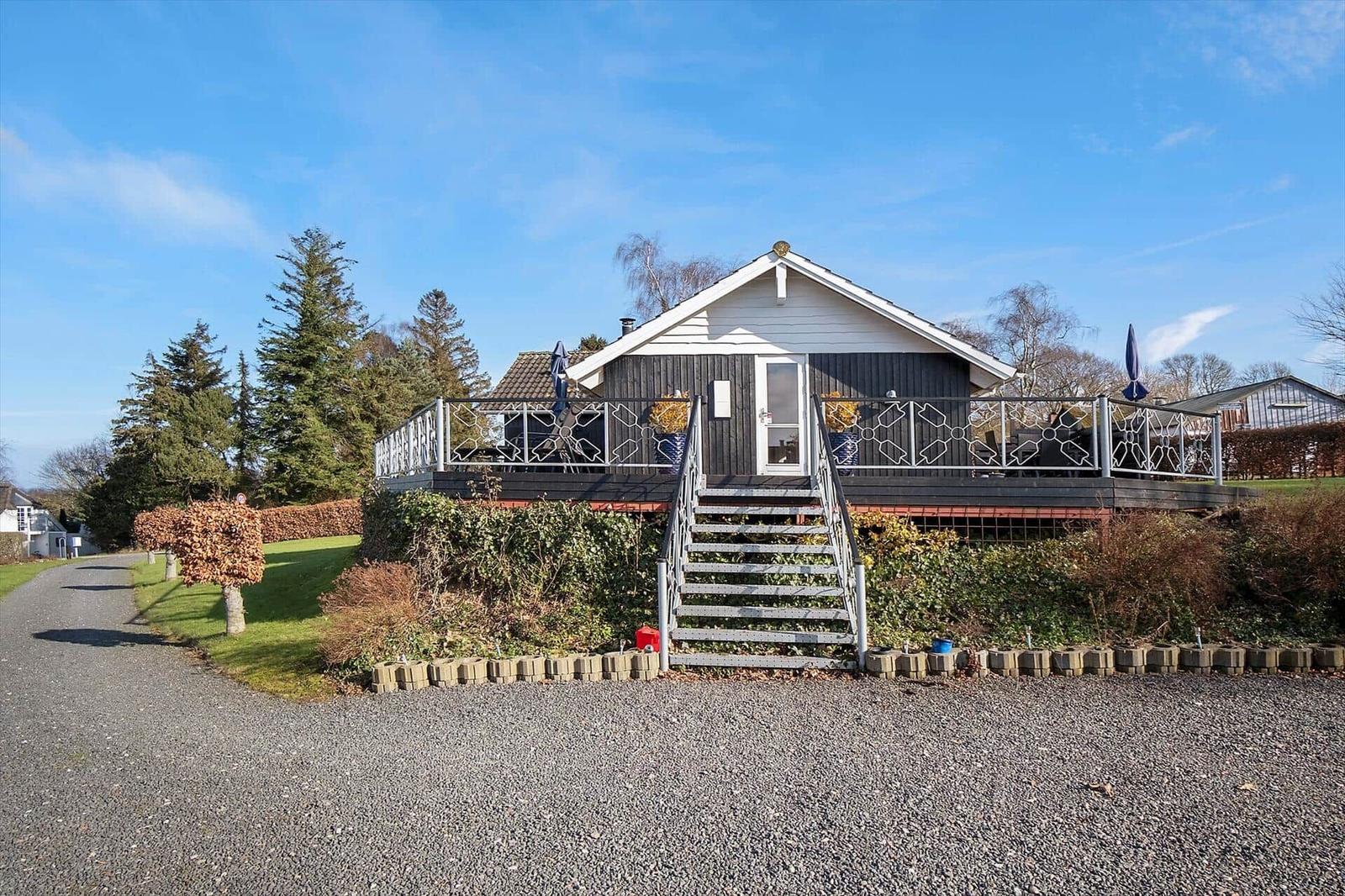 Haus mit Balkon, Treppe und Garten unter blauem Himmel.