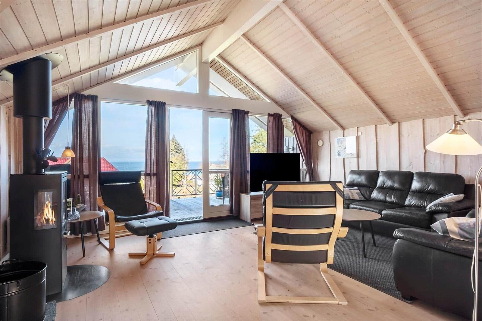 Wohnzimmer mit Holzdecke, Kamin, Sofa und Blick auf Balkon und Meer.