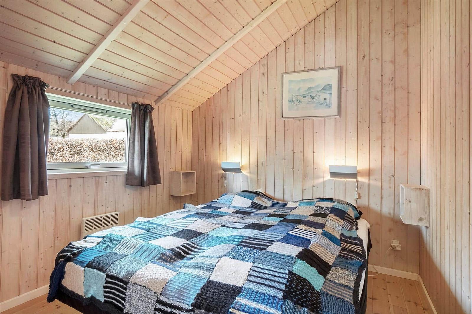 Schlafzimmer mit Holzwand, Bett mit buntem Decken und Fenster.