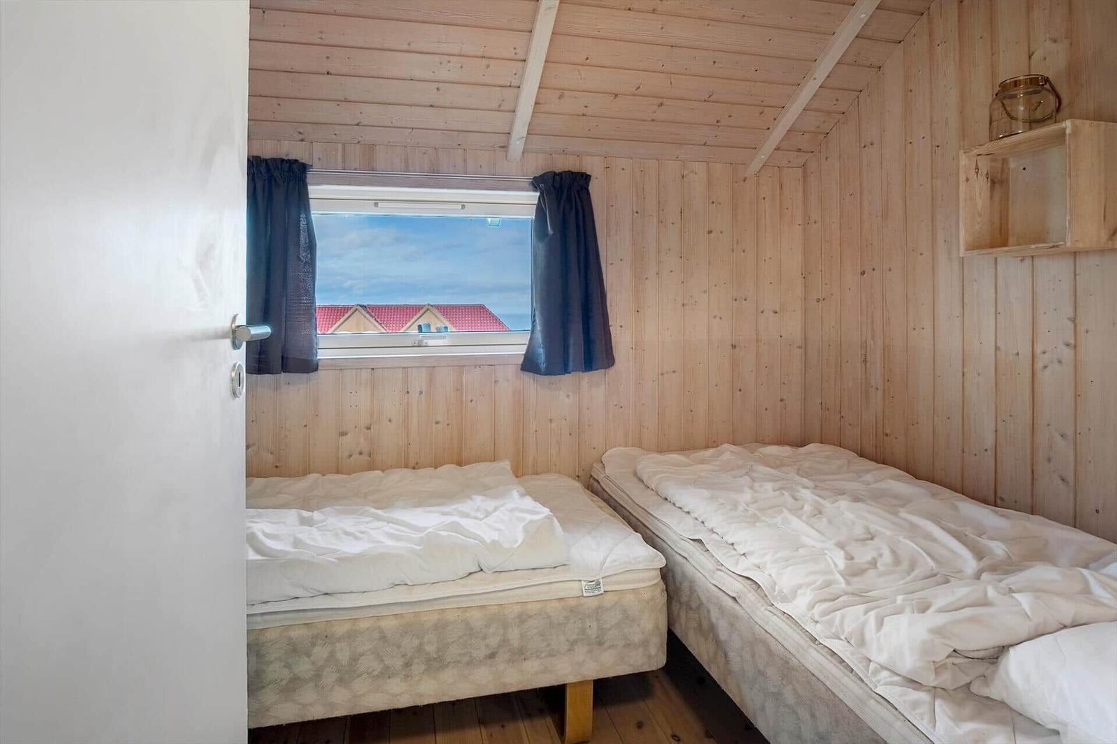 Zwei Betten in einem Holzhaus mit Fensterblick auf Dächer.